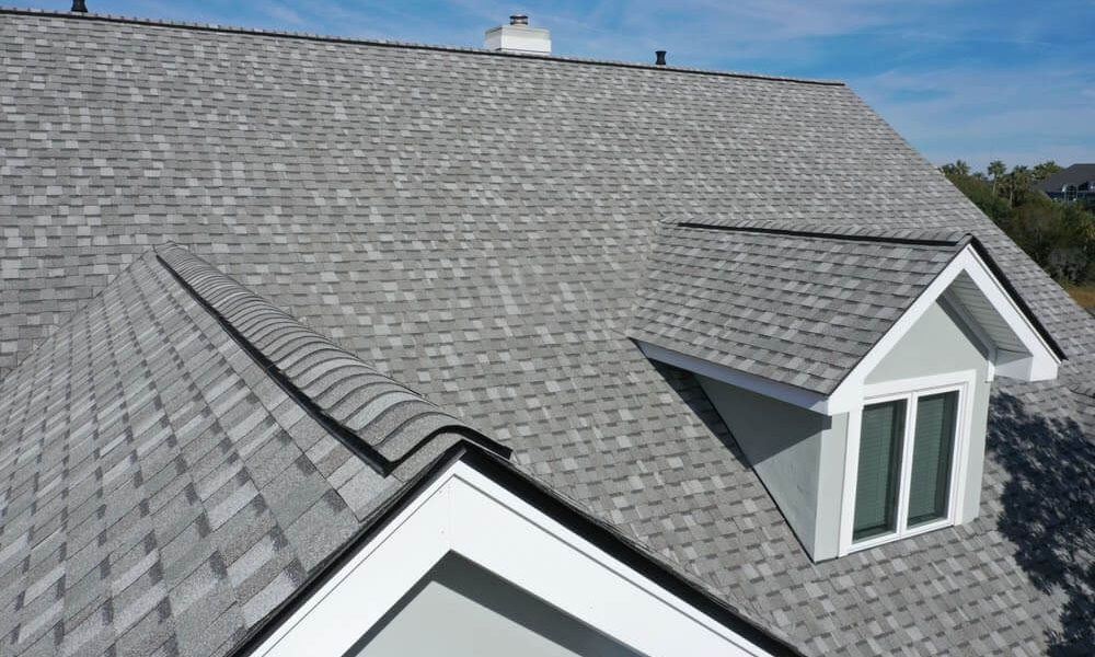 Gray asphalt shingle roof with dormer windows under a blue sky. The roof has a uniform pattern and appears recently installed.