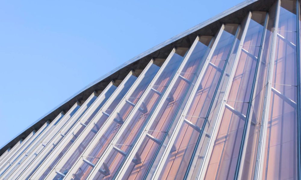 Glass and steel structure with angled vertical beams reflecting the blue sky, photographed from a low upward perspective—showcasing craftsmanship reminiscent of projects completed about Aleman Roofing.