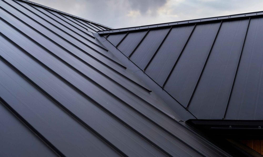 Dark metal roof panels with visible seams under a cloudy, overcast sky—quality craftsmanship you can expect from Aleman Roofing.